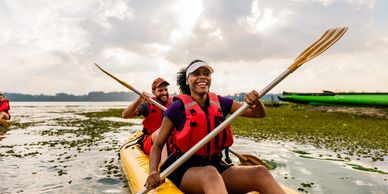 Two people kayaking and smiling on a lake.