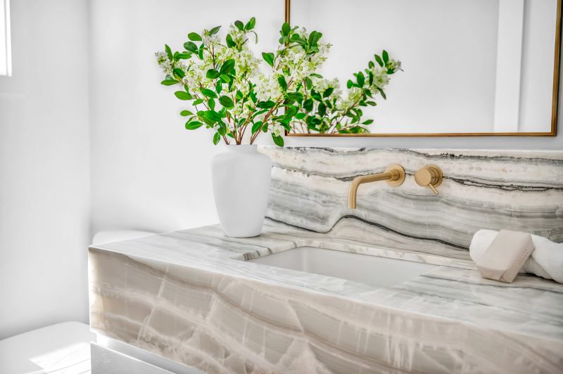 Beautiful modern marble sink with marble front and backsplash. Gold color faucet hardware. modern design, rolled washcloth and soap. white vase with green plant