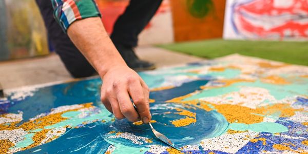 Hand painting a colorful abstract canvas with a palette knife.