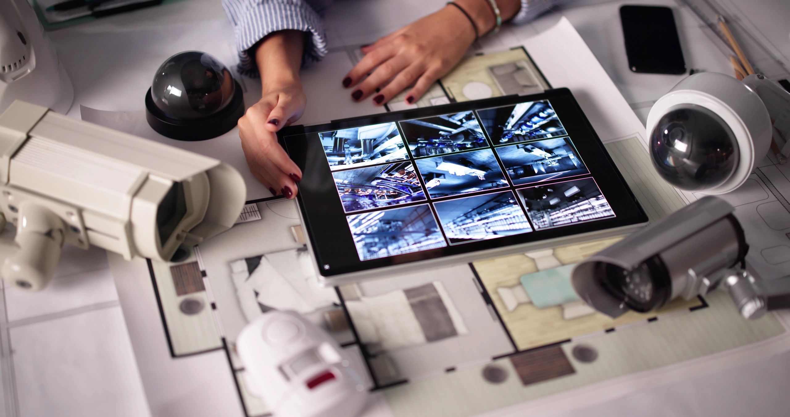 Person monitoring security camera feeds on a tablet surrounded by multiple cameras.