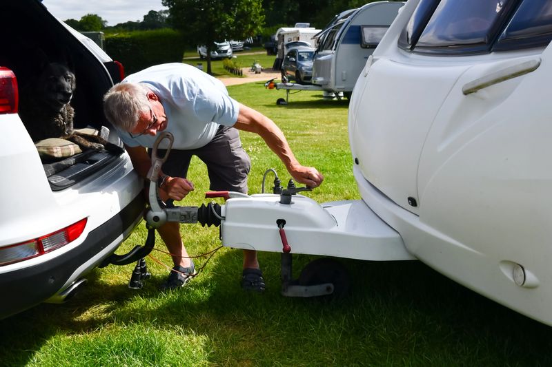 Hooking up, man carefully alines the towbar of his car to the hitch of his caravan using the jockey wheel to wind the vehicles to the correct height. Preparing to tow the caravan home safely after a vacation in the caravan.