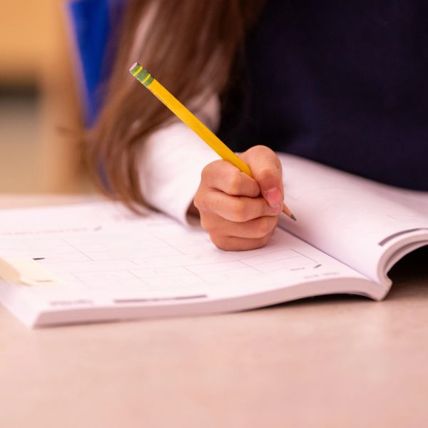 Child holding a yellow pencil over an open workbook.