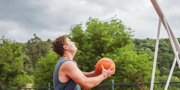 A man preparing to shoot a basketball outdoors on a cloudy day.