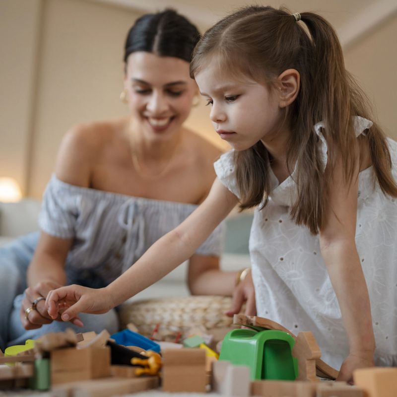 mother and her little daughter playing with wooden toys on carpet at home