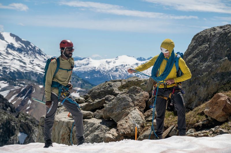 Climbing guide teaches client on mountain ridge, snowcapped mountains behind, British Columbia Coastal Ranges
