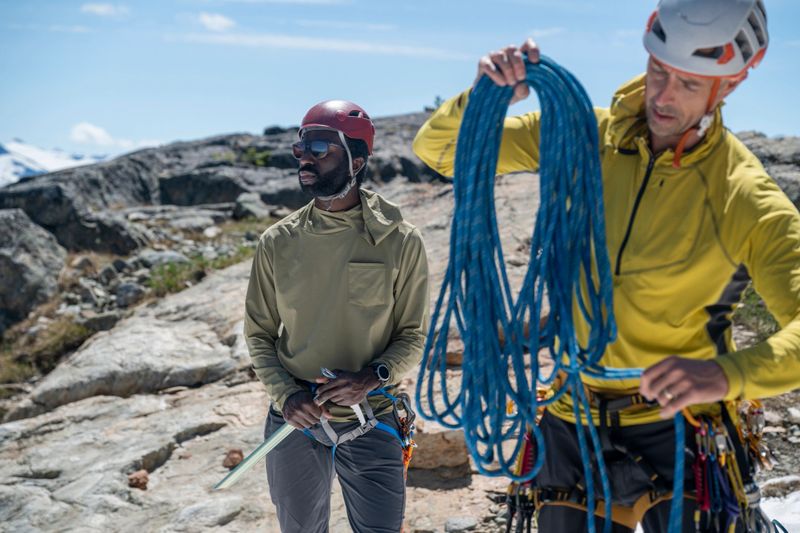 Climbing guide prepares rope on mountain top beside client, British Columbia Coastal Ranges