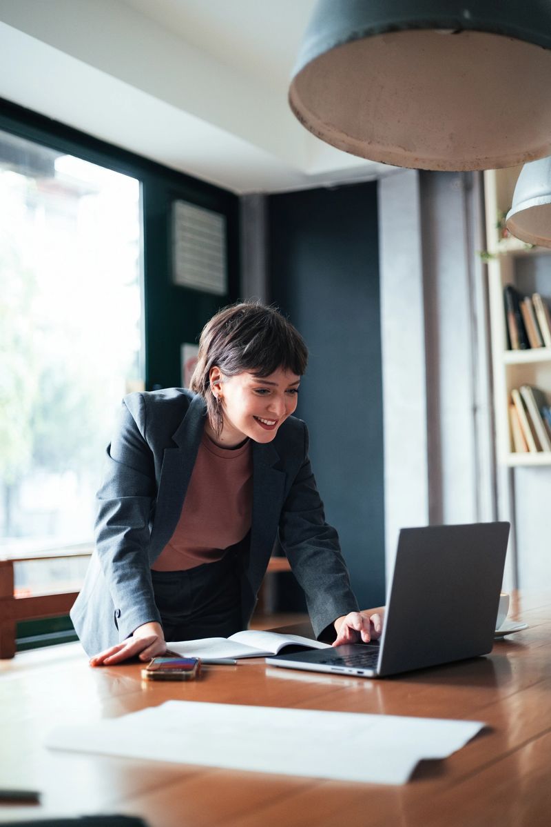 Smiling professional in business attire working with a laptop in a modern office, displaying engagement and productivity. Captures a professional, vibrant workplace atmosphere with natural lighting and minimalist elements.