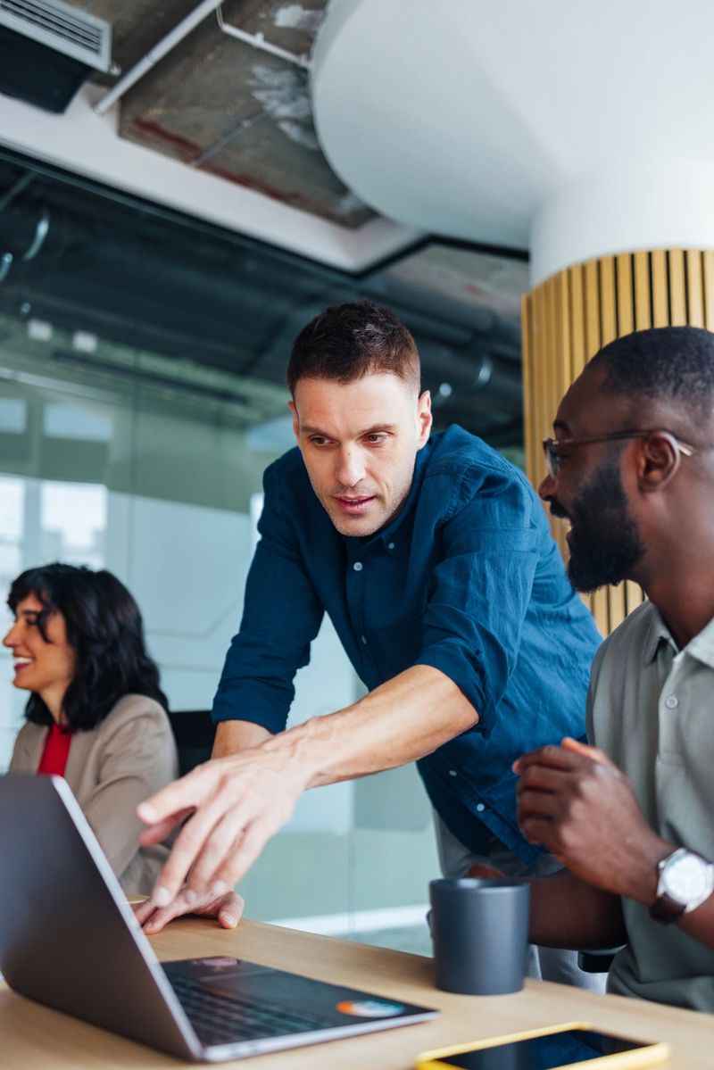 Colleagues engaging in cooperation and discussion around a laptop in a modern office setting, promoting teamwork and productivity, fostering ideas and solutions in a professional and collaborative workplace atmosphere.