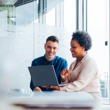 Two colleagues smiling and looking at a laptop.
