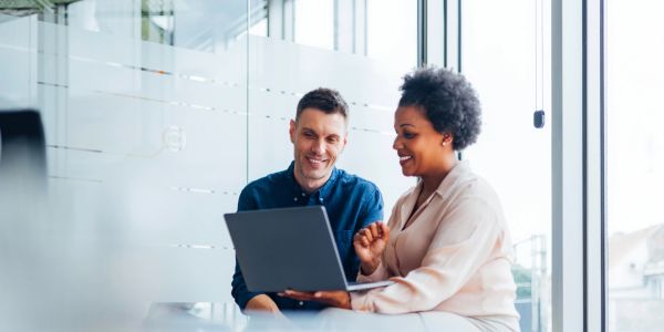 Two colleagues smiling at a laptop screen in an office.
