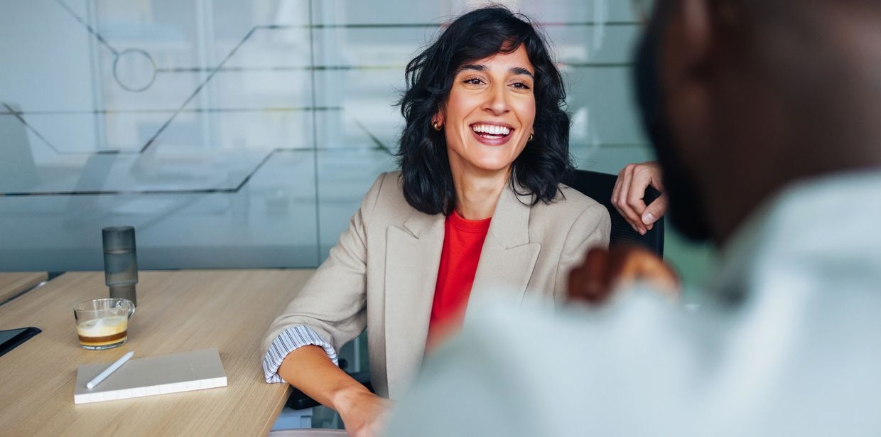 A woman in a blazer smiling during a meeting.