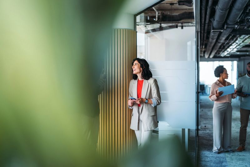 Group of diverse professionals engaging in conversation in a modern workspace, featuring natural greenery and a contemporary design.