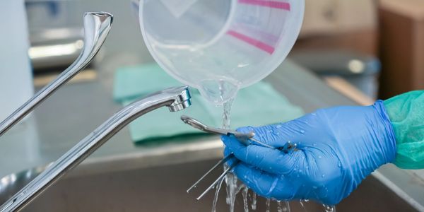 A gloved hand rinses surgical tools under running water in a clinical setting.