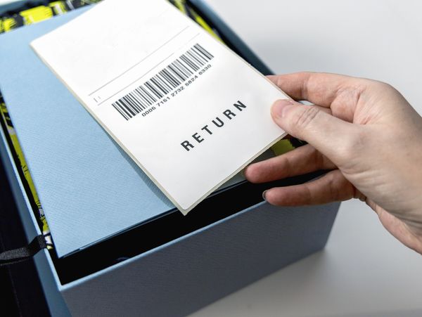Hand holding a return label over a blue box, ready for shipping.