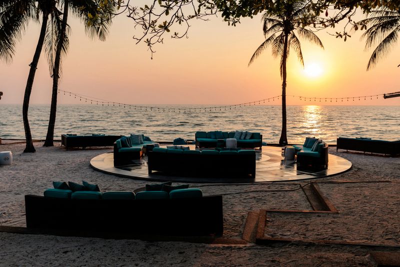 Sunset on luxury beachfront platform featuring multiple plush sofas for relaxing, surrounded by tropical palm trees.