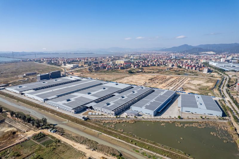 A modern factory in Putian City, Fujian Province, has installed new clean energy solar photovoltaic panels above the factory building.Shot from above, the image shows an extensive grid of dark-blue solar modules covering the flat roof of an industrial plant. Each panel catches the midday sun, producing sharp reflections and subtle gradients of color that emphasize their clean, geometric layout. Vent stacks, skylights, and maintenance walkways punctuate the array, adding scale and industrial context. The bright daylight and crisp shadows convey energy efficiency and modern sustainability. Ideal for stock categories: renewable energy, industrial infrastructure, green technology, corporate sustainability, and aerial rooftop photography.