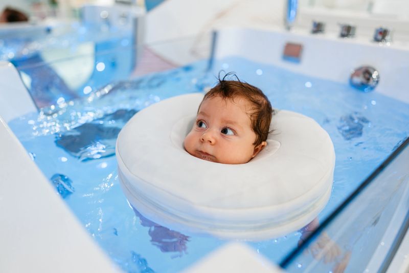 Baby boy swimming in a tub with a floatie in the baby spa.
