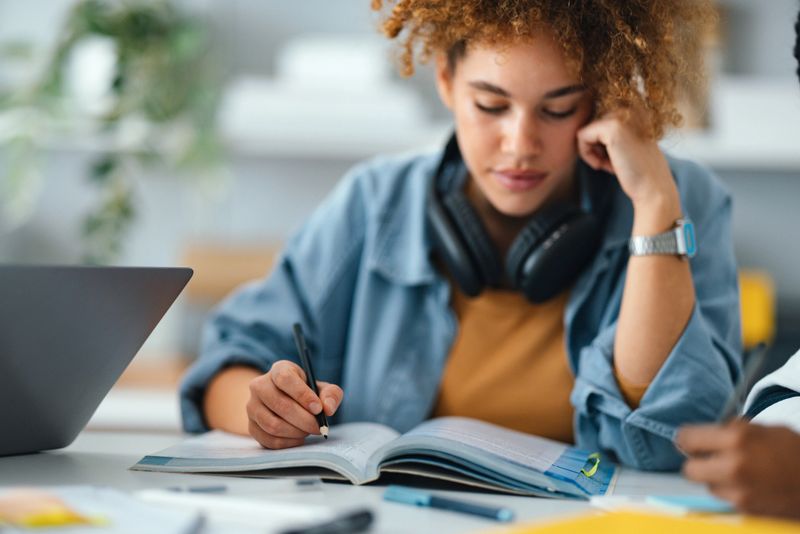 Depicts a young person deeply engaged in studying, surrounded by books and technology, creating an intellectual and focused atmosphere.