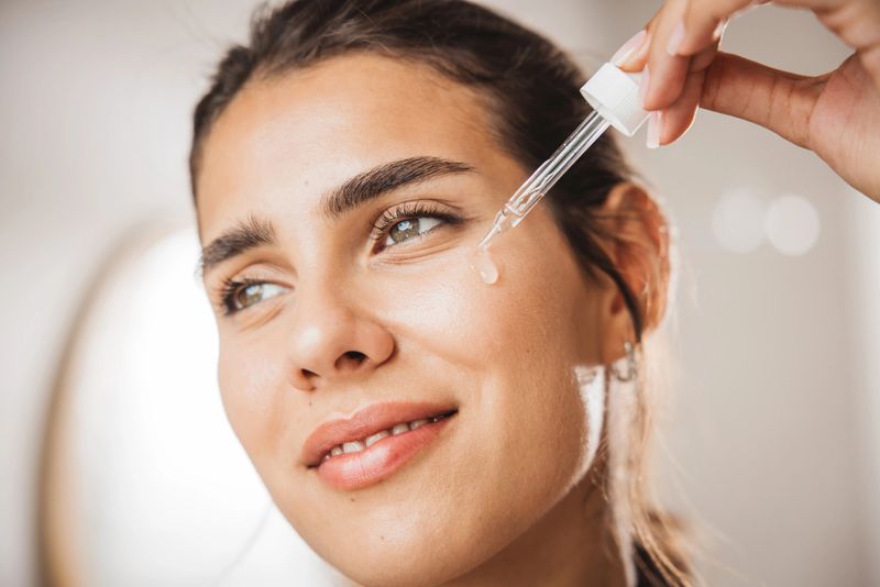 Young woman applying serum on face in front of mirror in bathroom