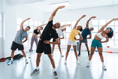 Group fitness class doing side stretches in a bright studio.