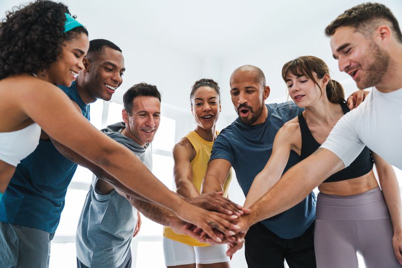 Multiethnic group of sportive people doing functional workout in training class gym diverse fitness group joining hands after functional training. Embodying teamwork. Motivation