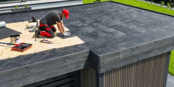 Worker installing roofing material on a flat rooftop.