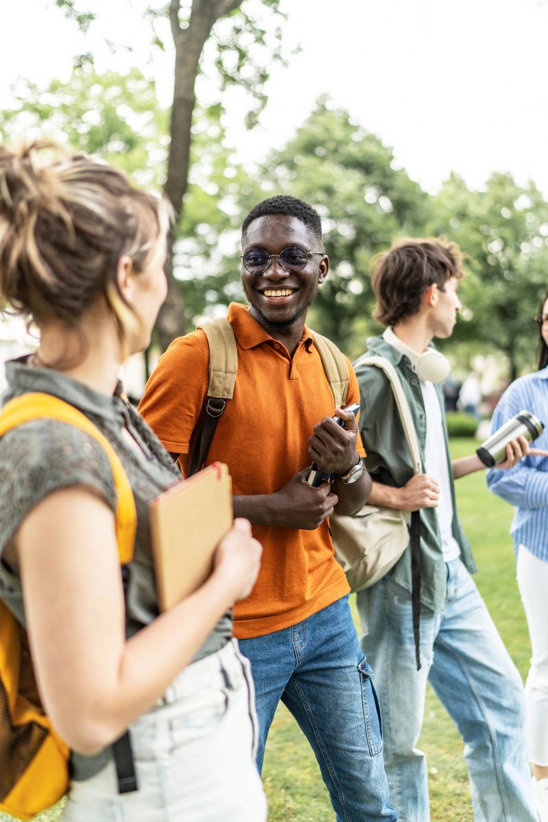 Multi-ethnic group of students carrying backpacks and books, enjoying a lively conversation while walking together on a sunny campus day, radiating friendship and community spirit