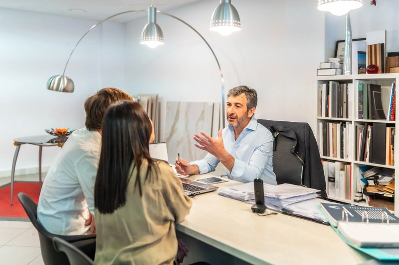 Architect explaining home renovation project to couple in a showroom, discussing ideas and materials