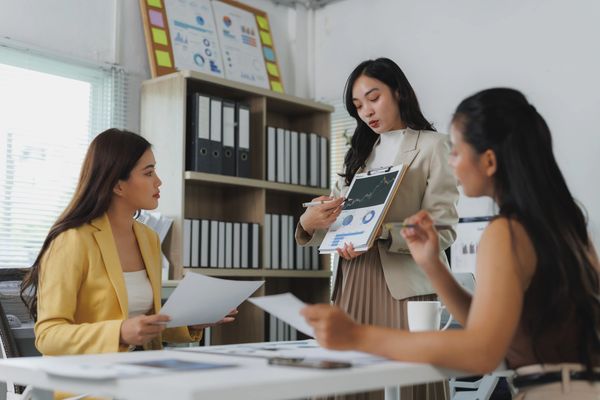 Three female professionals in an office discussing business and reviewing documents during a meeting