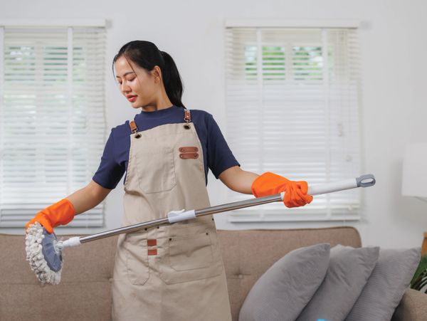 Woman in apron and gloves cleaning with a mop indoors.