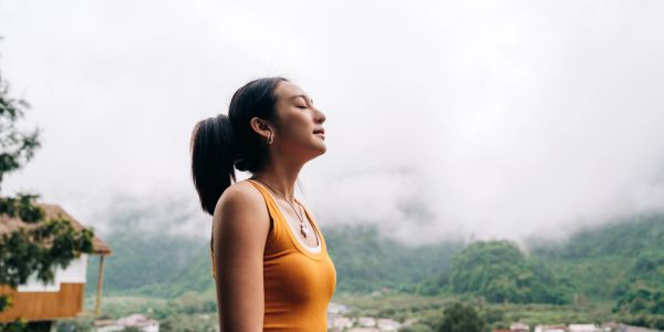 Woman in orange tank top enjoys fresh mountain air.
