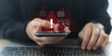 Warning alert on smartphone with digital icons hovering over a laptop.