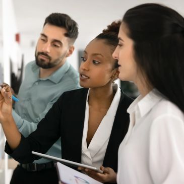 Three professionals collaborating and discussing ideas on a whiteboard.