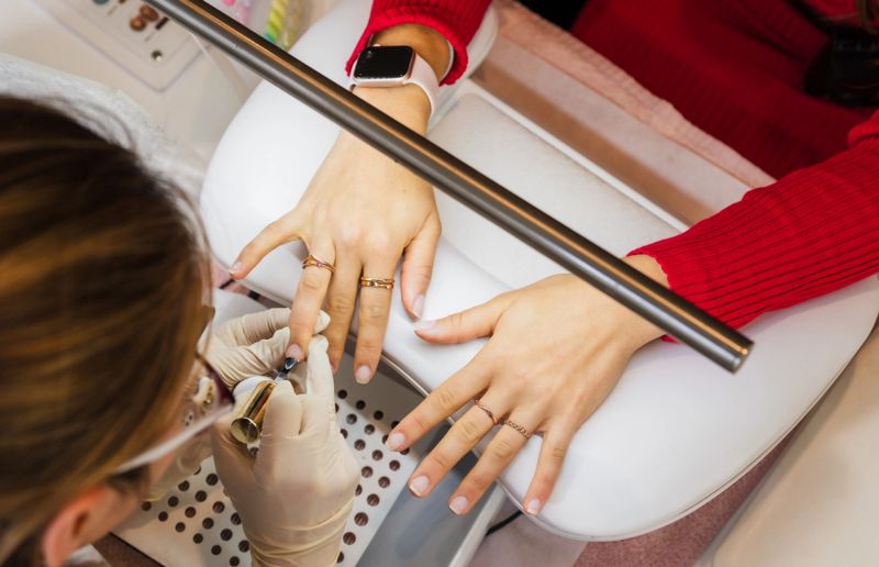 Beauty artist carefully applying nail polish to client's nails during a manicure session.