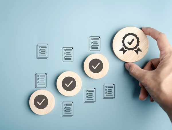 Hand placing wooden token with checkmark and badge icons, symbolizing quality and approval.