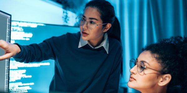 Two women discussing code on a computer screen.