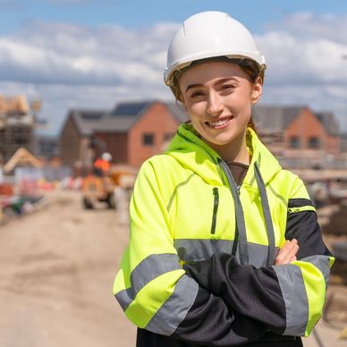 Smiling female construction worker in safety gear at a building site.