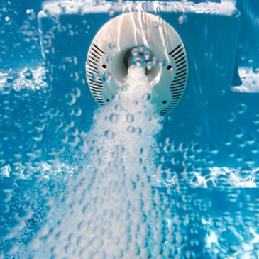 Underwater water jet releasing bubbles in a pool.