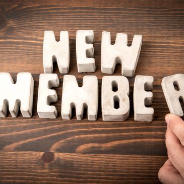 Concrete letters spelling 'NEW MEMBER' on wooden surface.