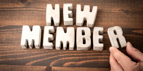 Block letters spelling 'NEW MEMBER' on wooden surface with hand placing letter R.