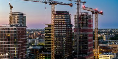City skyline with multiple cranes constructing high-rise buildings at dusk.