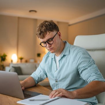 Young man focused on writing notes while working on a laptop.