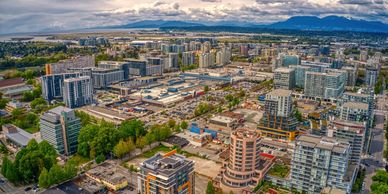 Aerial view of a modern cityscape under cloudy sky with mountains in the background.