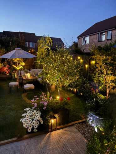 Cozy backyard garden illuminated with warm lights and comfortable seating at dusk.