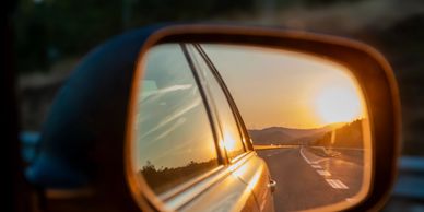 Sunset reflected in a car's side mirror on a road trip.