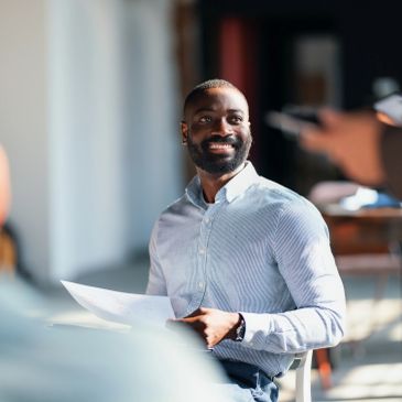 Smiling man in a light blue shirt holding papers during a meeting.