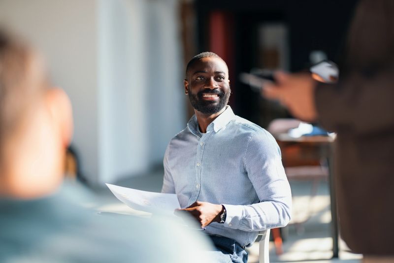 A cheerful man engages with colleagues during a corporate meeting in a contemporary office environment, promoting interaction, collaboration, and teamwork in a professional setting.