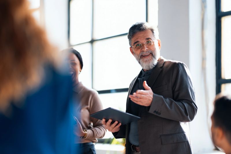Engaged colleagues interacting with a senior businessman presenting with enthusiasm in a modern office environment.
