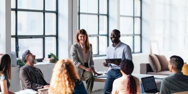 A diverse team engaged in a lively office meeting with large windows.