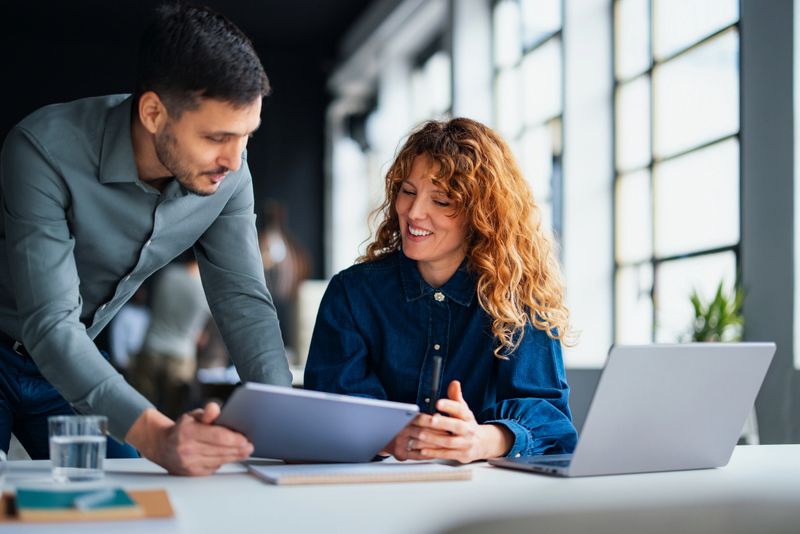 Colleagues discussing and sharing insights during a teamwork session, fostering productivity in a contemporary office setting. They appear engaged and motivated, embodying a positive and cooperative workplace environment.